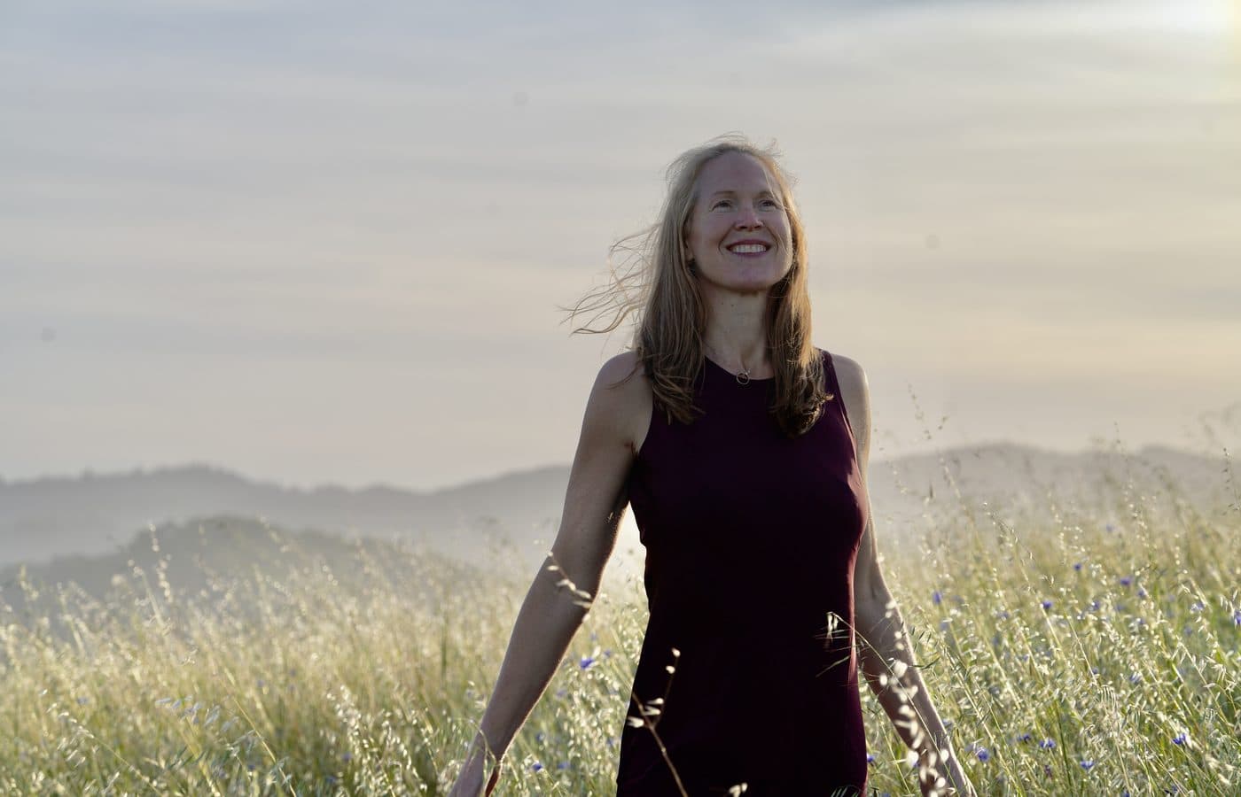 Alexis in a wide, green natural field that supports rhythm, integration, and return.